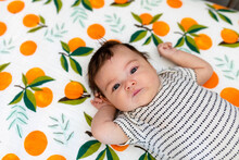 Newborn Baby Lies On Clementine Sheets And Looks At Camera