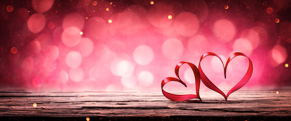 Wall Mural - two ribbon hearts on rustic wooden table with glowing bokeh background - valentines day