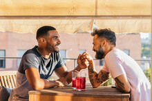 Interracial Gay Couple Having A Drink And Having Fun On A Terrace