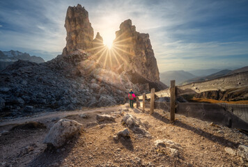 Wall Mural - Woman near wooden fence on the mountain trail and stones at sunset in autumn in Dolomites, Italy. Sporty girl on the path and high rocks in fall. Colorful landscape with cliffs, sun, blue sky. Hiking