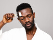 © ohlamour studio/Stocksy - Man with closed eyes using beauty device