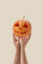 Carved Pumpkin Held By Woman's Hands On Beige.