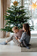 © Sergey Narevskih/Stocksy - Woman and child sitting under Christmas tree at home