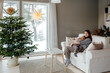 © Sergey Narevskih/Stocksy - Woman and child hugging on couch in room with Christmas tree at home
