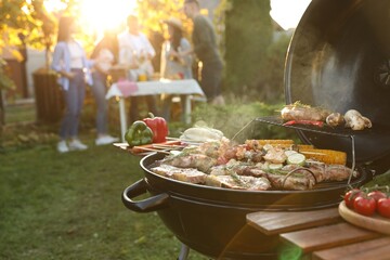 Group of friends having party outdoors. Focus on barbecue grill with food. Space for text