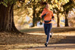 Happy female athlete jogging on autumn day in nature.