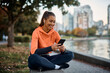 © Drazen - Young happy sportswoman texting on mobile phone while relaxing in park.