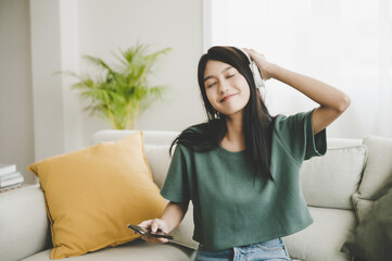 Poster - Asian young woman sitting on sofa. Happy female listening music and dancing in living room. She happy and relaxing at free time on weekend