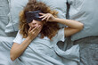 © Duet Postscriptum/Stocksy - Portrait of curly woman in sleep mask yawning in bed