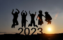 Happy Group Of People Celebrate Jump For New Year 2023. Concept For Win Victory. Silhouette Of Friends Jumps At Sunset Time On Mountains.