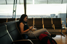 Woman At Airport Using Mobile Waiting At Boarding Gate