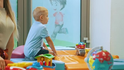 Wall Mural - full shot of a blond little boy playing with a bike in the playroom, kids activities concept. High quality 4k footage