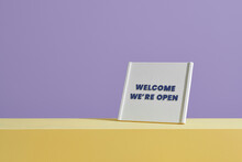 Welcome We're Open Sign On Table Over Purple