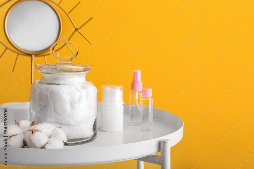 Container with soft cotton wool on table near yellow wall