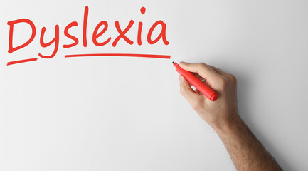 Man writing word Dyslexia on white background, closeup. Banner design