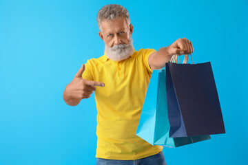 Sticker - Senior man pointing at shopping bags on blue background