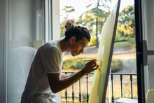 Concentrated Artist Painting A Canvas Near A Balcony In A Studio