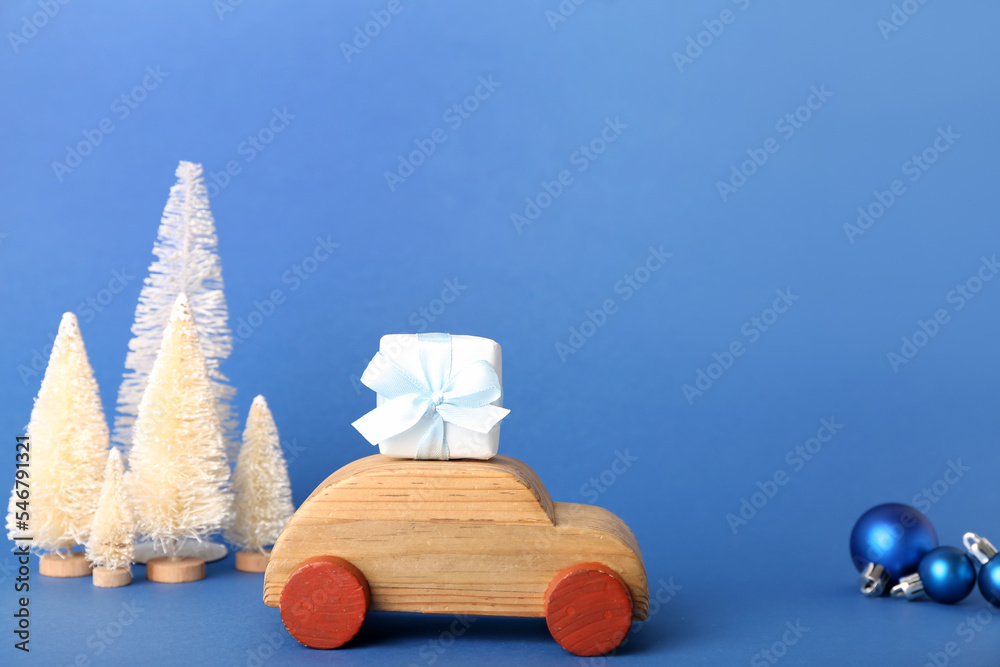 Toy car with Christmas trees and gift on blue background