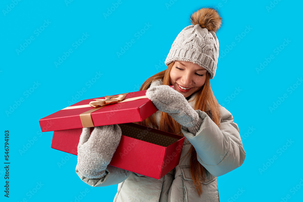 Young woman opening Christmas present on blue background