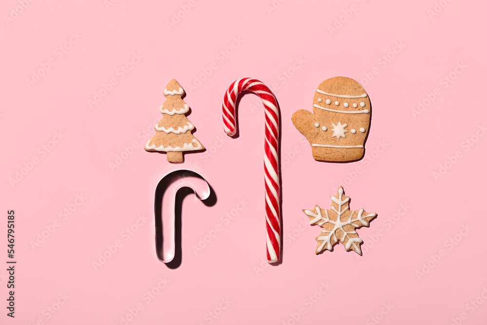 Composition with tasty Christmas cookies, candy cane and cutter on pink background