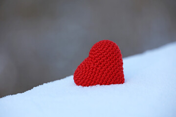 Wall Mural - Red knitted heart in the snow on blurred background. Symbol of romantic love, Valentine's card