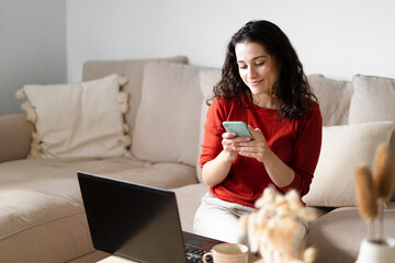 Young happy woman using the phone and  the computer sitting on the couch