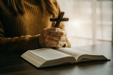 Close up of an open bible with a cross for morning devotion on a wooden table with window lights.