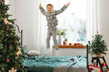Little Boy Jumping On Bed Near Christmas Tree