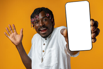 Excited young african man holding smartphone with white blank screen in hand on yellow studio background