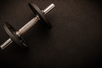 Loadable dumbbell on the floor at the gym. Top down view flat lay with bodybuilding equipment on a black background and empty space for text. Fitness, weight training or healthy lifestyle concept