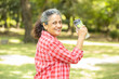 © GAJENDRRA BHATI  - Happy fitness senior indian woman resting holding water bottle after work out exercising in park summer morning outdoor portrait.
