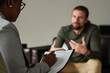 © AnnaStills - Close-up of African American psychotherapist making notes in card during psychotherapy with man