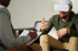 © AnnaStills - Close-up of therapist making notes in document during virtual session while man using VR glasses and talking about his impressions