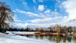 Wide-angle winter scene with lake, snowy shore and trees under blue cloudy sky