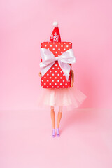 Wall Mural - Christmas shopping minimal concept. A doll with Xmas present in her hands on pink background