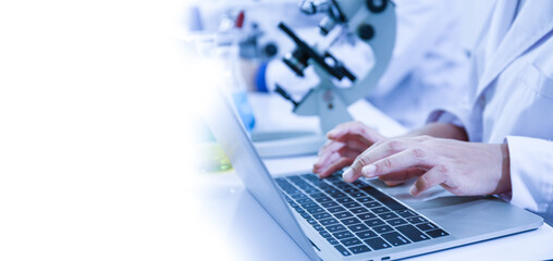 close-up view of a scientist or student using a laptop computer and a microscope. science concept