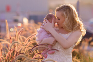 gentle blonde mother in a light long dress holds a newborn baby in her arms against the backdrop of 