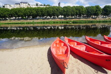 Red Kayak On The Sand By The Loire River Across The Town Of Chinon, France Reflecting In The Water
