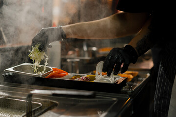 Burger cooking process - chef adding ingredients to bun in restaurant kitchen