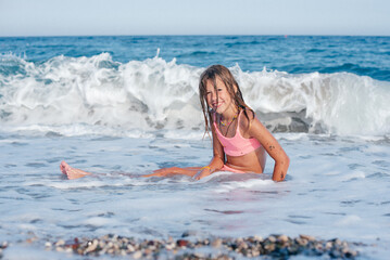 Little girl in the spray of waves at sea on a sunny day