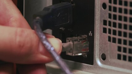 Poster - Close-up of a male hand inserting a network cable into a computer jack. The patch cord is connected to a computer network. Rear view of the computer.