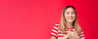 © Mix and Match Studio - Close-up tender touched young charming asian blond girl press palms heart thankful smiling broadly appreciate nice romantic compliments share heartwarming feelings, stand happy red background