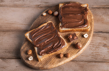 Wall Mural - Board of bread with chocolate paste and hazelnuts on wooden background. Popular desser food. Top view.