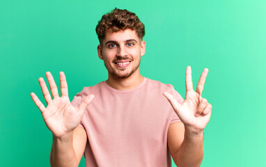 Wall Mural - young adult caucasian man smiling and looking friendly, showing number eight or eighth with hand forward, counting down