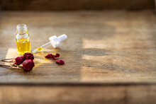 Essential Oil In A Small Glass Bottle With Dried Pink Roses In Bud On A Wood Background