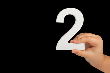 Aufkleber - Close-up hand holding a white number 2 on a black background. Number two isolate on black background in child's hand.