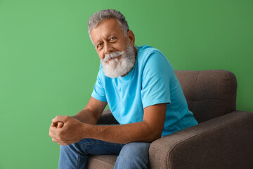 Sticker - Senior man sitting in armchair on green background