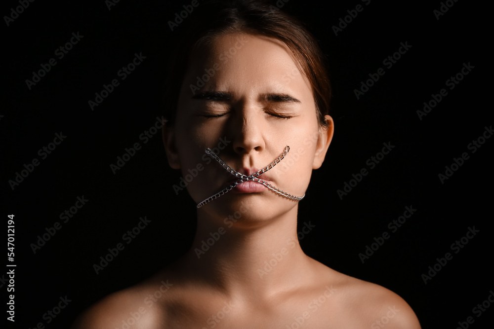 Young woman with chain on mouth against dark background. Censorship concept