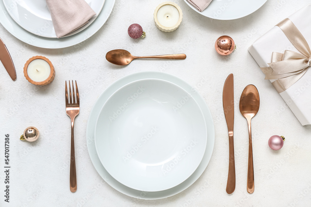 Beautiful table setting with Christmas balls, gift and candles on white background