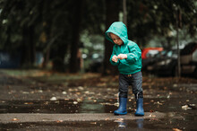 Happy Boy Playing Outside On A Rainy Day Wearing Rubber Boots And Jacket